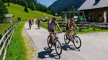 A group of cyclists on a paved path with a wooden fence on one side and a building with a sloped roof in the background.