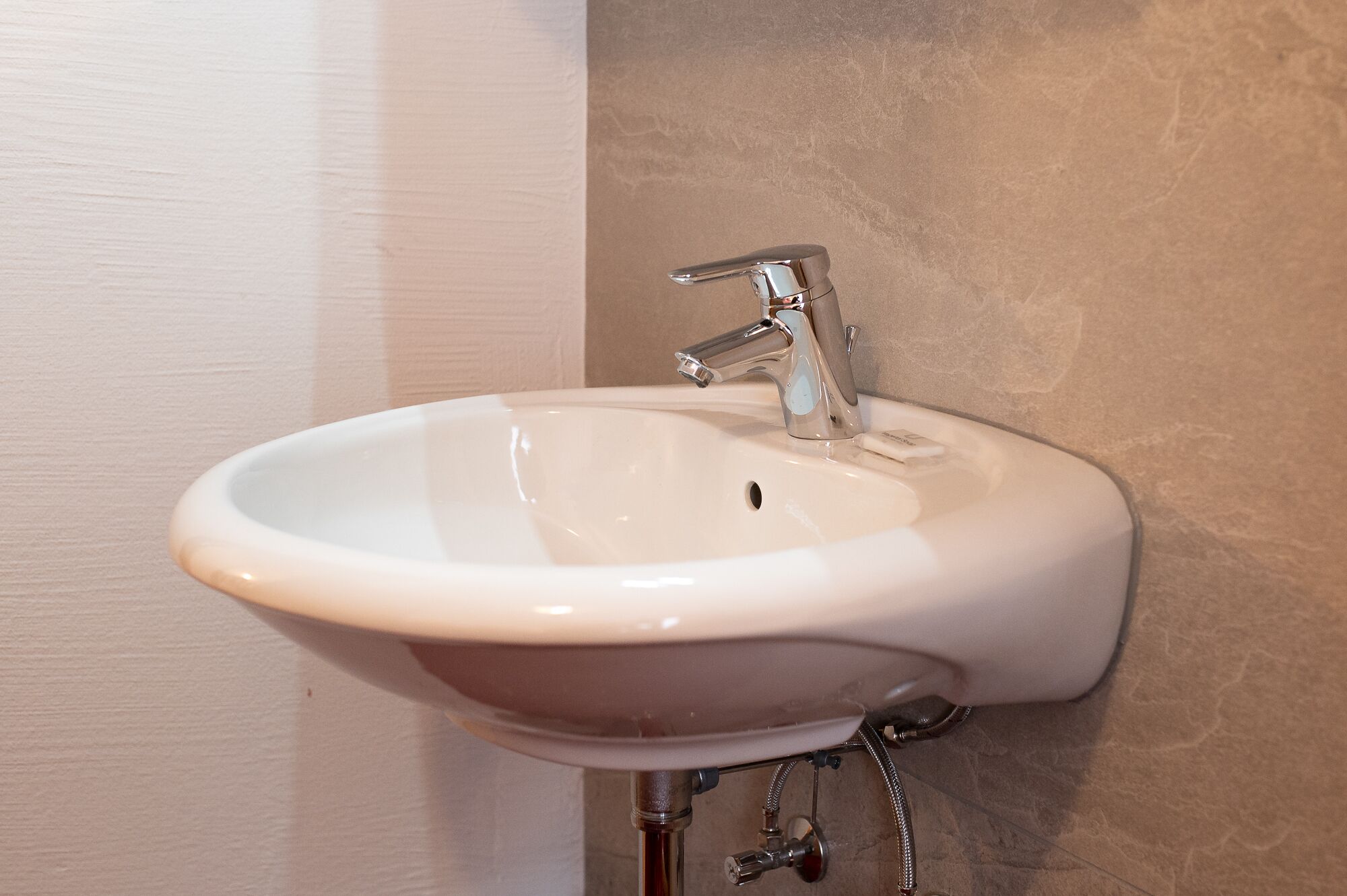 Un lavamanos de cerámica blanca con un grifo de un mando, instalado en una pared color crema.