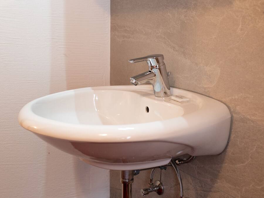 A white ceramic sink with a single-handle faucet mounted on a beige wall.