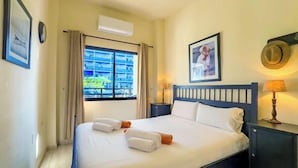 A neatly made bed with white linens and towels, a bedside lamp, a framed picture on the wall, and a window with curtains. - Skol 130 - 1-Bedroom Apartment with Sea Views in Marbella Centre (Marbella)