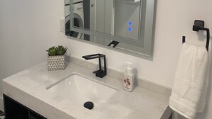 Casa de banho com um espelho grande, uma pia, um porta-toalhas e uma pequena planta num vaso.