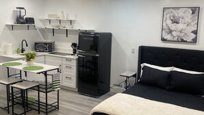 Quarto compacto com cama, cozinha compacta, área de refeições e ventoinha no teto.