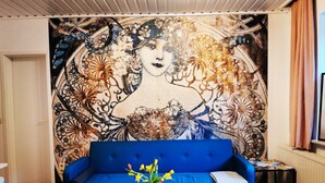 A room with a blue sofa, a glass coffee table with a chess set, and a wall mural. - Apartment 01 Rauenstein (Rathen)