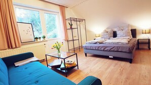 A bedroom with a bed, a sofa, a bedside table with a lamp, a window with curtains, and a radiator. - Apartment 01 Rauenstein (Rathen)