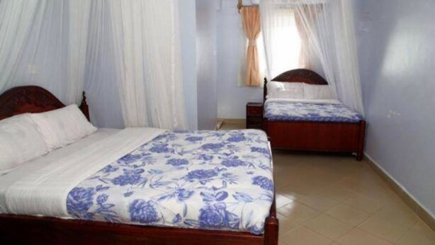 A bedroom with two beds, each with a canopy, and a nightstand between them. - Leopard View Hotel (Nakuru)