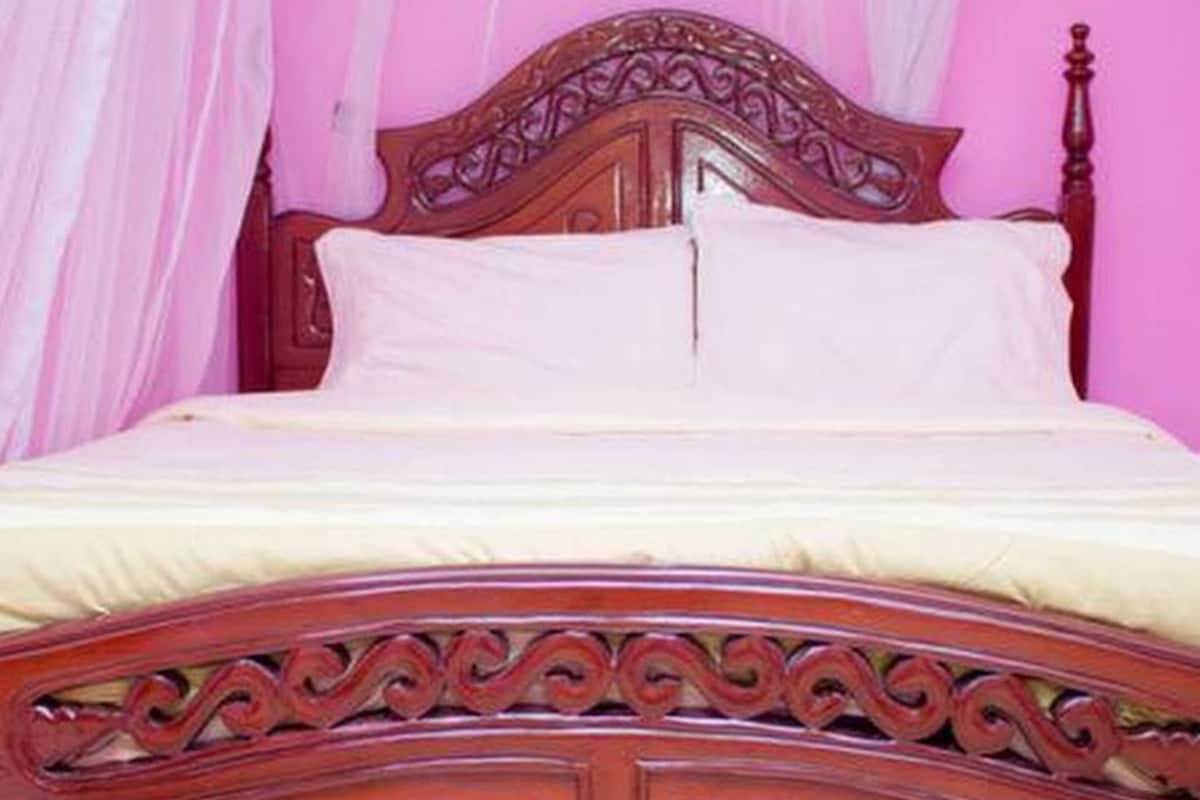 Un lit en bois orné de sculptures complexes et doté d’une tête de lit, placé contre un mur rose.