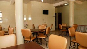 A conference room with multiple tables and chairs, a flat-screen TV mounted on the wall, and a door leading to another room. - Leopard View Hotel (Nakuru)