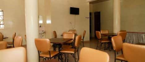 Un salón de conferencias con varias mesas y sillas, un televisor de pantalla plana montado en la pared y una puerta que da a otra sala.