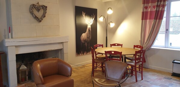 Un coin repas avec une table ronde et des chaises rouges, une cheminée et un luminaire fixé au mur.