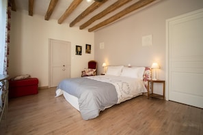 Une chambre à coucher avec un lit, un plancher en bois, un banc rouge, une porte et deux lampes fixées au mur.