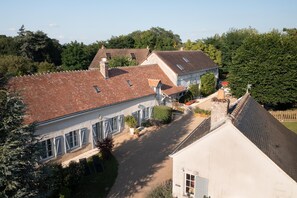 Une grande maison avec un toit recouvert de tuiles rouges, plusieurs cheminées et un jardin bien entretenu.
