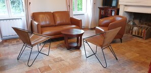 Een woonkamer met een bruine leren bank, twee fauteuils en een kleine houten salontafel.