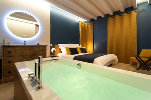 Une chambre moderne avec une grande baignoire, une commode en bois, un miroir rond et un lit avec une literie jaune et noire.