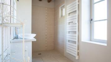 Une salle de bain avec un lavabo blanc, un porte-serviettes blanc, une douche avec une porte blanche et une fenêtre laissant entrer la lumière naturelle.