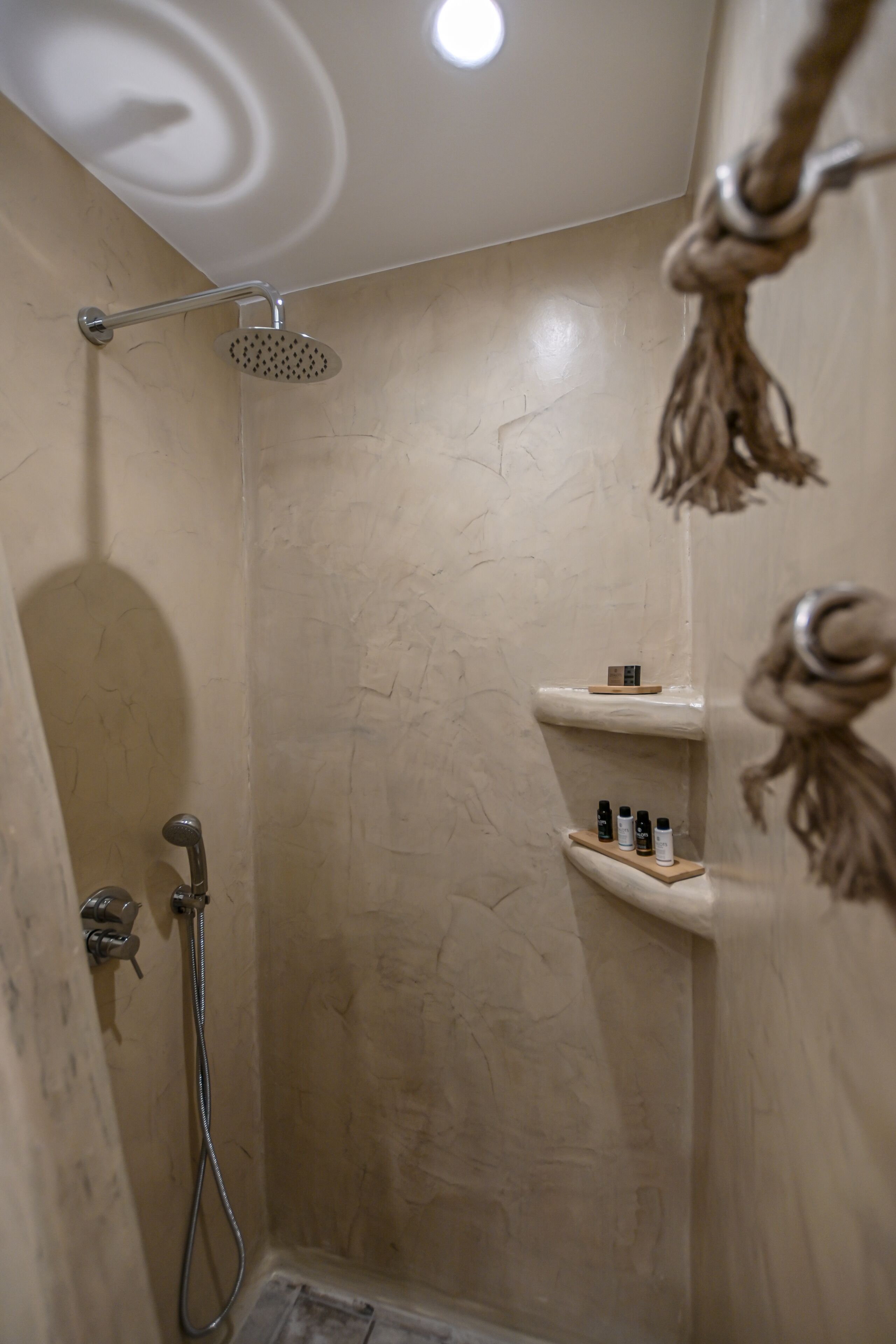 Ducha con cabezal de ducha de mano, grifo empotrado en la pared y repisa con artículos de aseo.