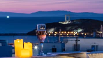 Un balcon avec une bougie, un verre de vin et une vue sur la mer et les montagnes au crépuscule.