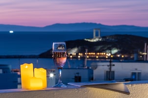 Un balcón con una vela, una copa de vino y vistas al mar y las montañas al atardecer.