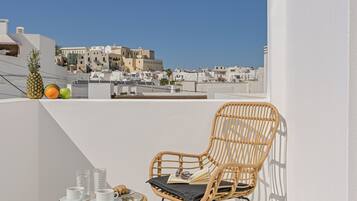 Un balcon avec un fauteuil en osier, une petite table ronde avec une tasse et une soucoupe blanches, et un ananas.