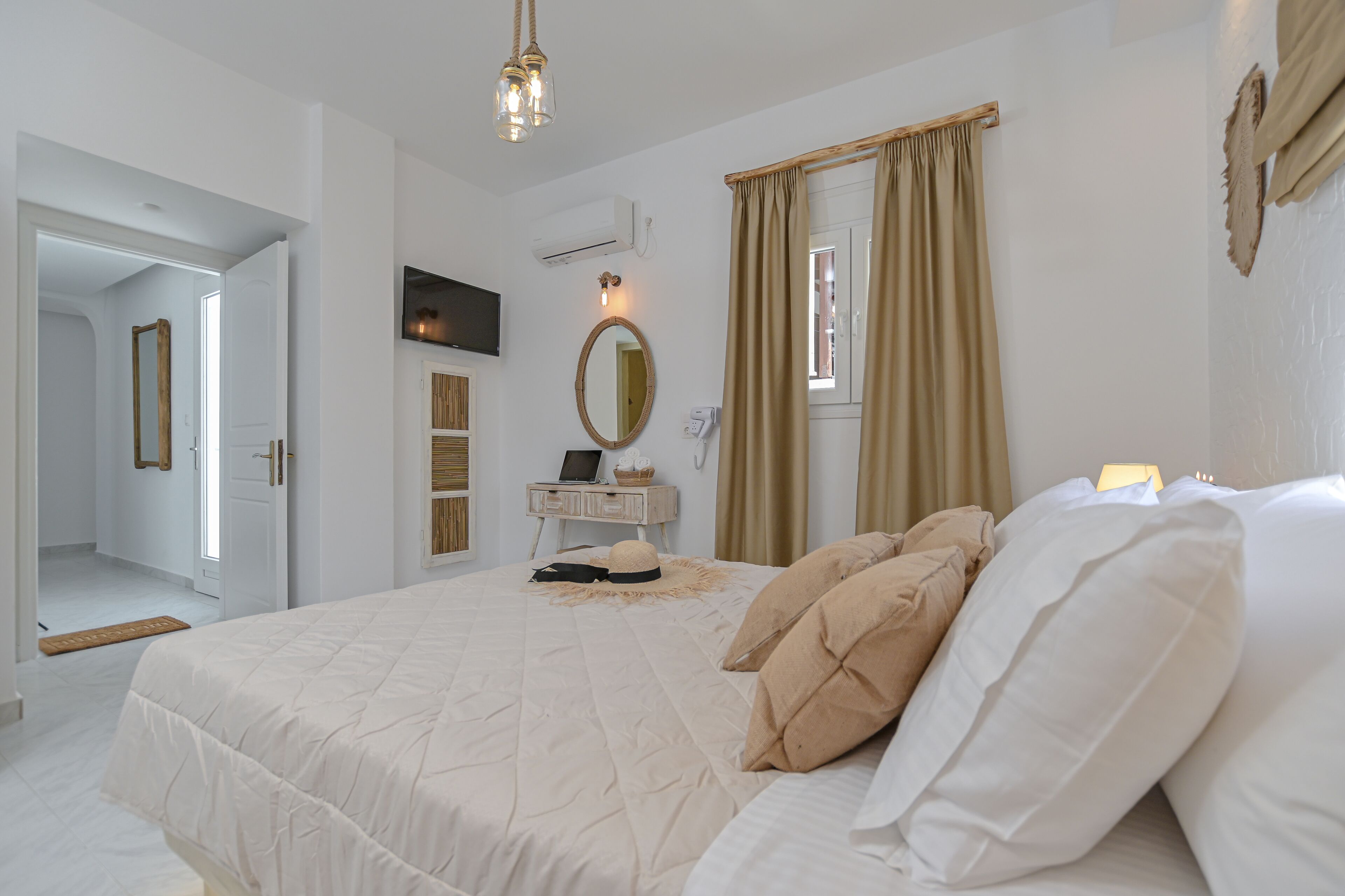 Un dormitorio con una cama grande, una mesita de noche con lámpara, un espejo y una ventana con cortinas.