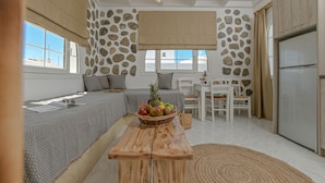 A modern kitchen with a stone wall, a wooden table with a fruit basket, and a dining area with white furniture. - Naxian Horizon (Naxos)