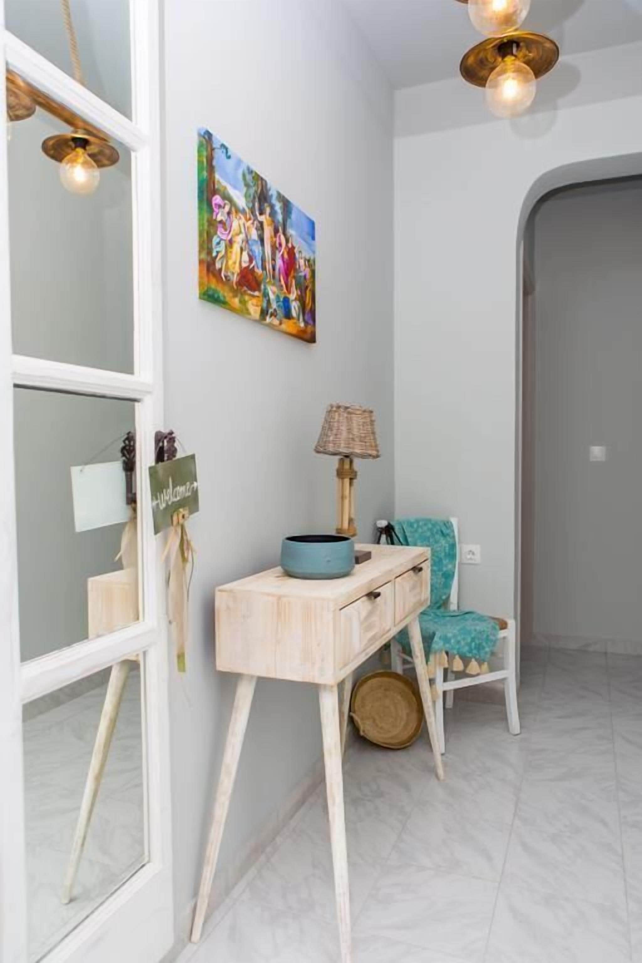 Un pasillo con una consola de madera, una lámpara, una silla y un cuadro en la pared.