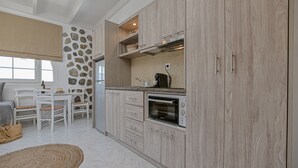 A modern kitchen with light wood cabinetry, a built-in oven, and a stone accent wall. - Naxian Horizon (Naxos)
