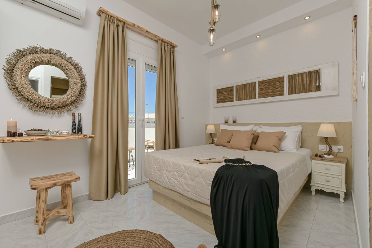 Quarto moderno com uma cama grande, um banquinho de madeira, um espelho e uma mesa de cabeceira com abajur.