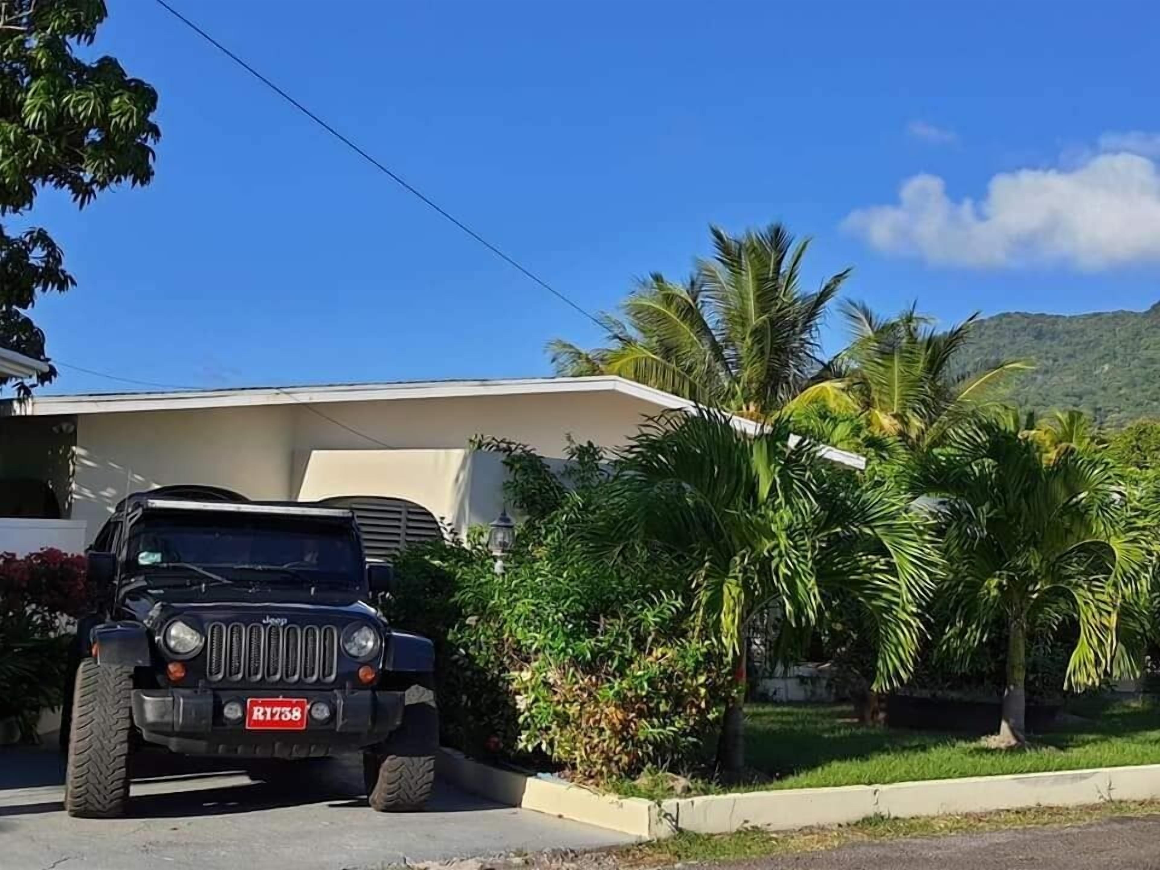 Un vehículo todoterreno negro estacionado en una entrada de casa, con una vivienda y palmeras al fondo.