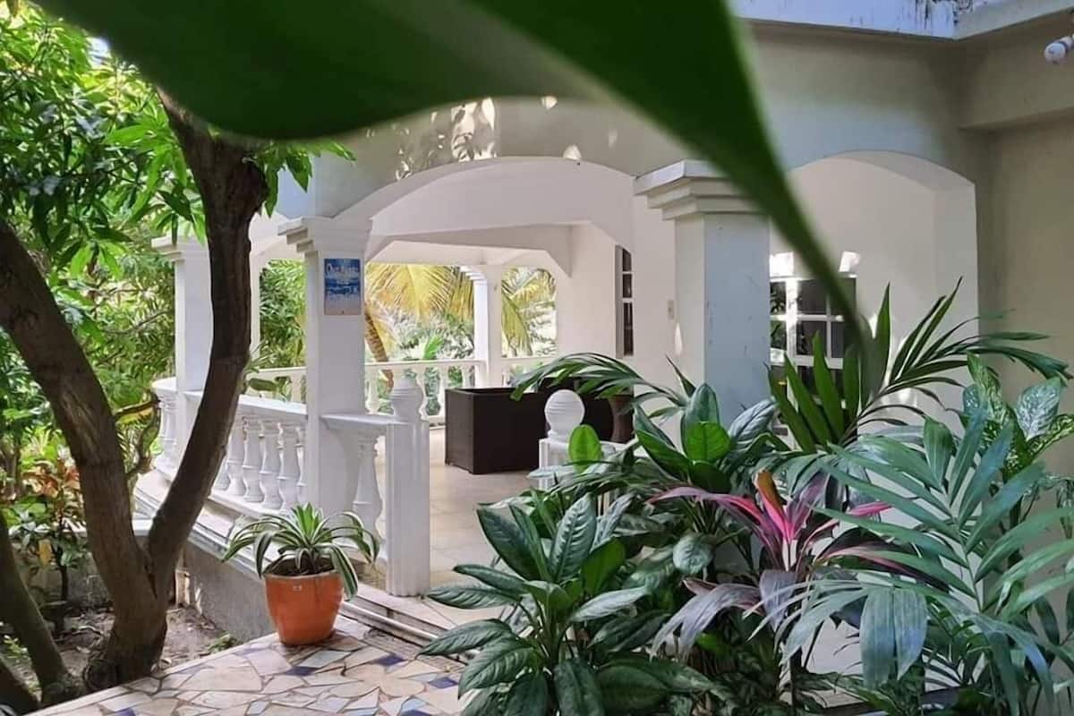A covered outdoor area with a white structure, potted plants, and a tiled floor.