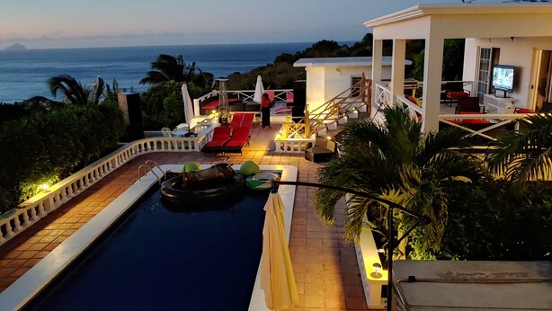 A pool area with a view of the ocean, a lounge with red chairs, and a white building with a staircase. - Chez Mango Villas (Old Towne)