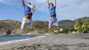 Two people jumping on a beach with a mountainous backdrop and a clear sky. - Chez Mango Villas (Old Towne)