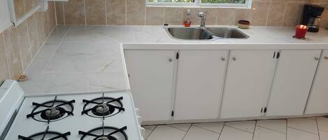 A kitchen with white cabinets, a gas stove, a sink, and a window with a view of greenery.