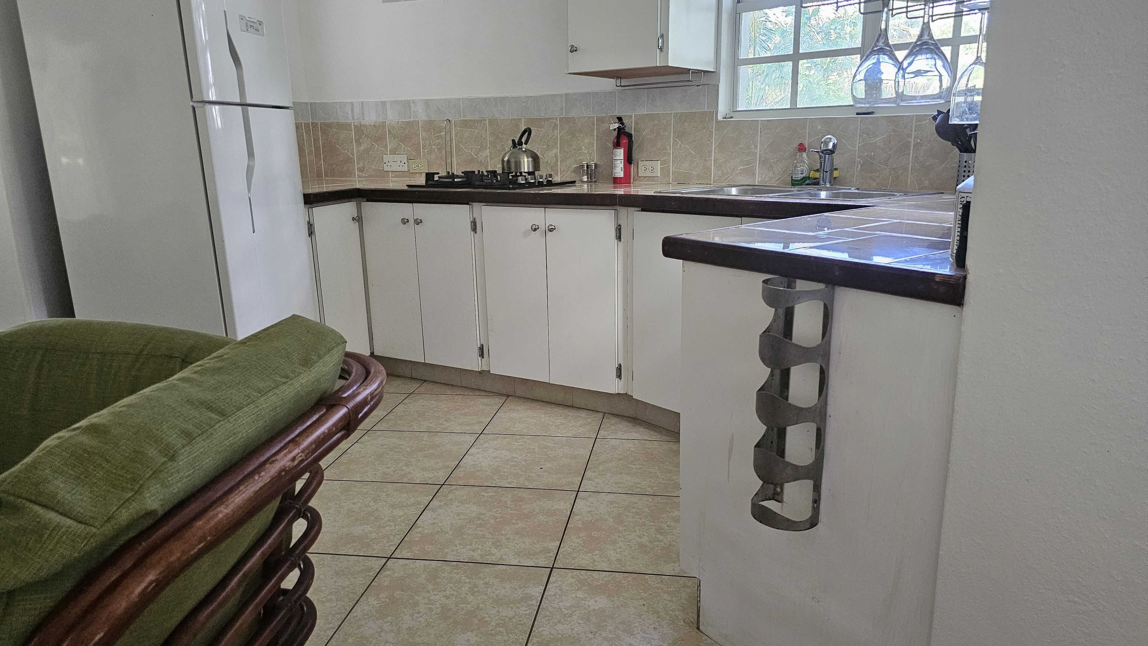 Una cocina con armarios blancos, una estufa a gas, un fregadero y un ventanal con vistas a la vegetación.