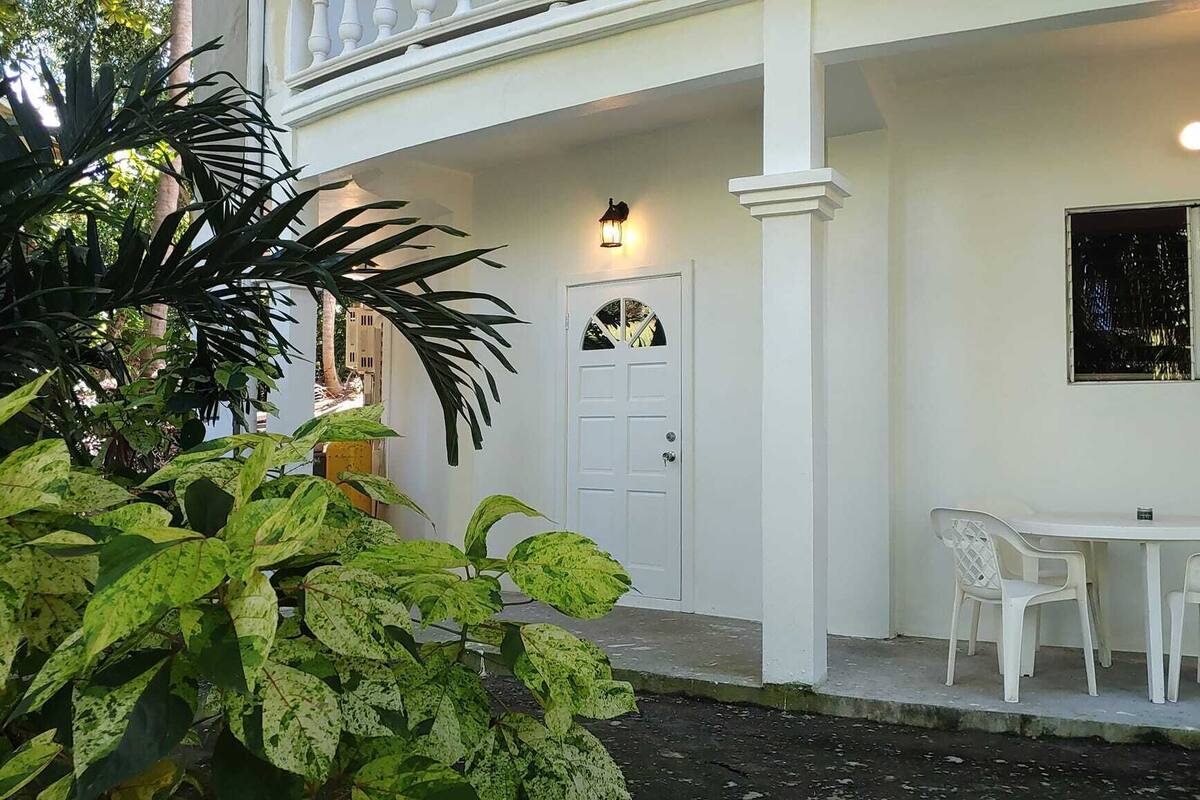 A white building with a door, a small table with chairs, and potted plants.
