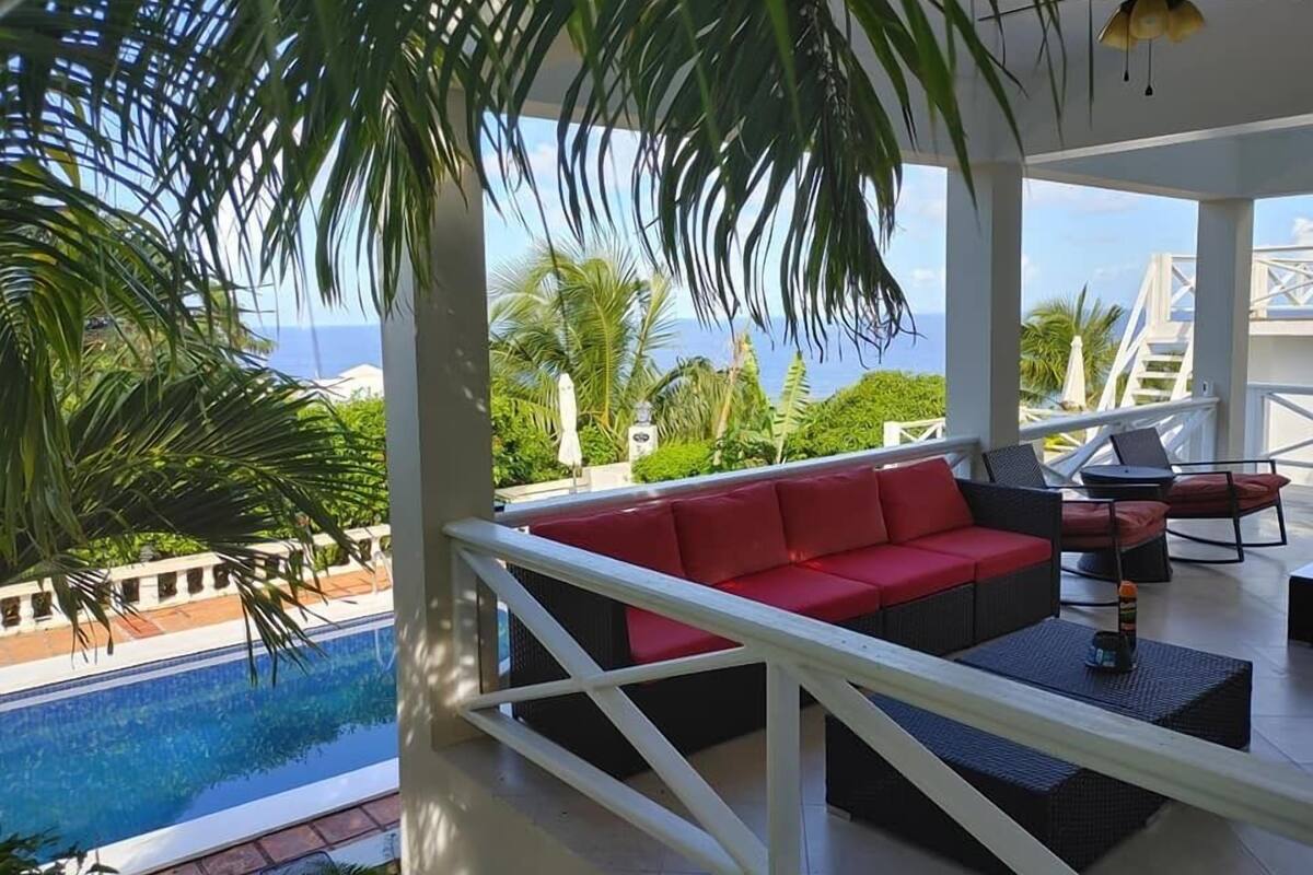 A poolside area with a red sofa and black chairs, overlooking a swimming pool and a view of the ocean.
