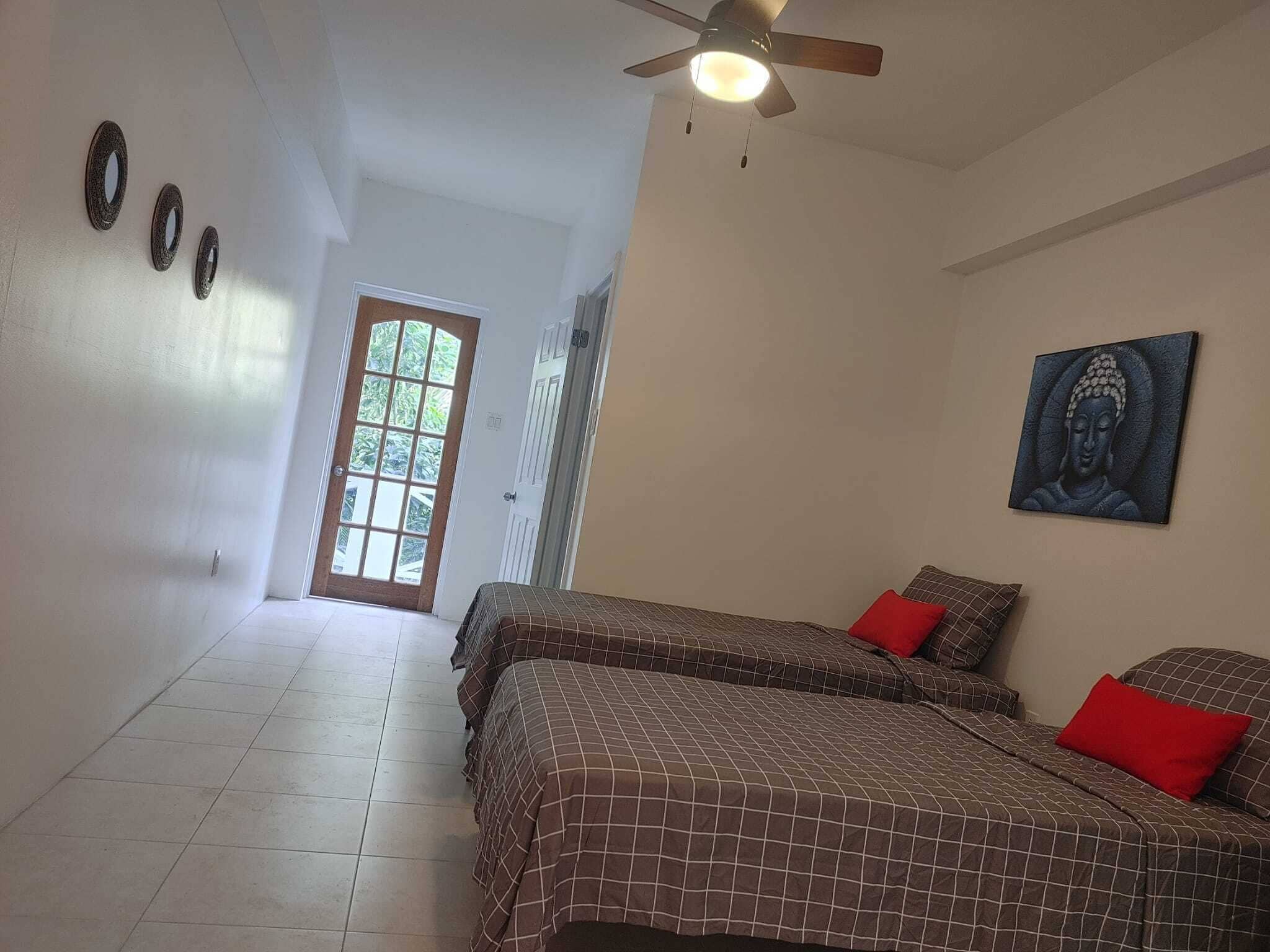 A bedroom with two beds, a ceiling fan, a Buddha painting, and a door leading to a balcony.