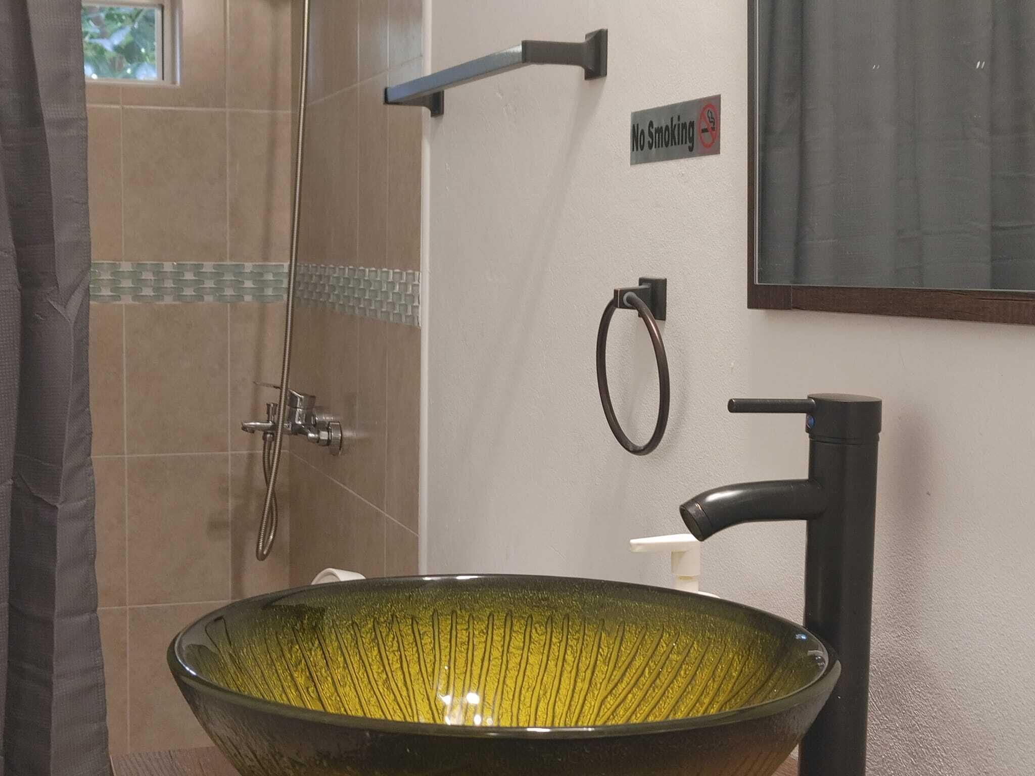 A bathroom with a large green ceramic sink, a shower, a towel ring, and a 'No Smoking' sign.