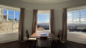 A dining area with a large table and chairs, a view of the city through large windows, and curtains on the windows. - The Portland Apartment, 2 beds with parking (Bath)