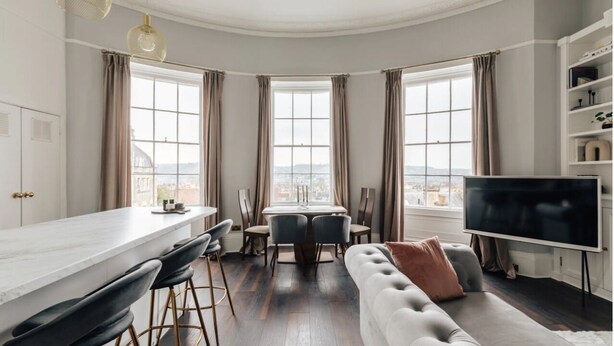 A modern living room with a dining area, large windows, and a flat-screen TV. - The Portland Apartment, 2 beds with parking (Bath)