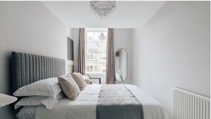 A modern bedroom with a large bed, a mirror, and a view of buildings through the window. - The Portland Apartment, 2 beds with parking (Bath)