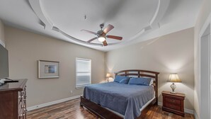 A bedroom with a bed, nightstand, lamp, ceiling fan, and wooden flooring. - Ground Floor Bayside Beauty Walk to the Beach (South Padre Island)