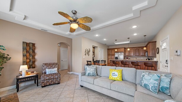A spacious living room with a grey sofa, a patterned armchair, and a ceiling fan. - Ground Floor Bayside Beauty Walk to the Beach (South Padre Island)