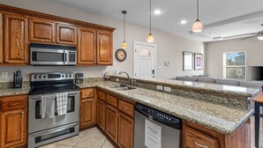 A modern kitchen with granite countertops, wooden cabinets, stainless steel appliances, and pendant lighting. - Ground Floor Bayside Beauty Walk to the Beach (South Padre Island)