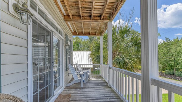 A wooden deck with a covered porch, white railings, and a wicker chair. - 4 Bedroom, 3 1/2 Bath Dog-Friendly Beach Home with Private Pool (Garden City Beach)