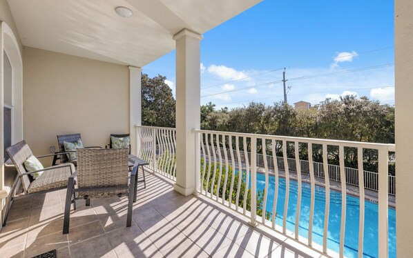 A balcony with a pool, outdoor furniture, and a view of trees and buildings.