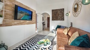 Uma sala de estar moderna com uma TV de tela plana, um sofá de couro marrom, um tapete estampado e um objeto decorativo na parede.