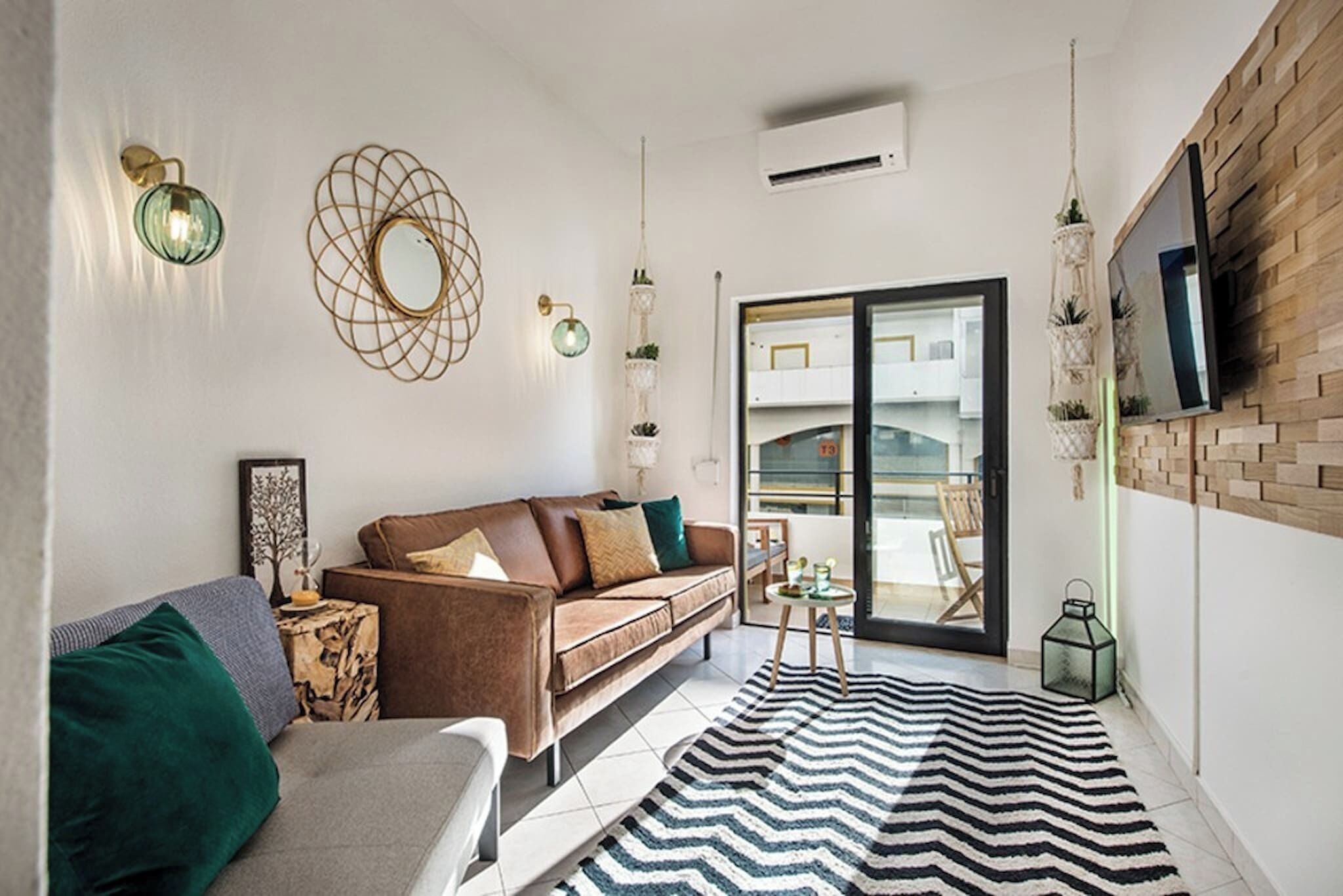 A modern living room with a brown sofa, a striped rug, and a large window with a view of a balcony.