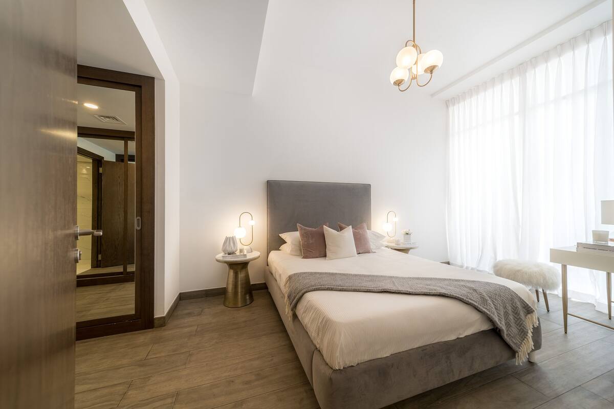 Ein modernes Schlafzimmer mit einem großen Bett, Nachttischen mit Lampen, einem Schreibtisch und einem großen Fenster mit Vorhängen.