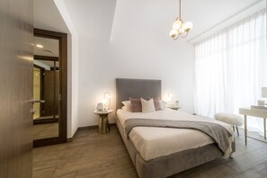 A modern bedroom with a large bed, bedside tables with lamps, a desk, and a large window with curtains. - Hameni By Zaya (Dubai)