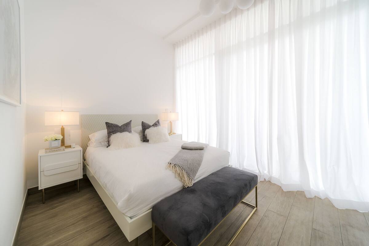 Ein modernes Schlafzimmer mit einem großen Bett, Nachttischlampen, einem Beistelltisch und einer Bank.
